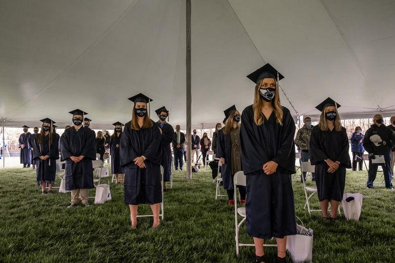 Graduates in caps and gowns standing under large white tent.